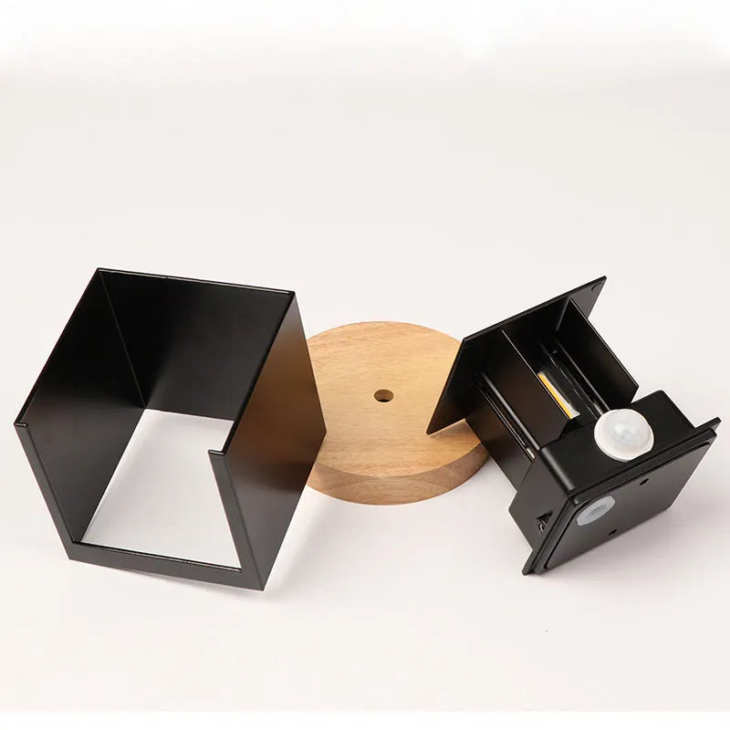 Black aluminium square wall lamp mounted on a corridor wall, showing 100mm size and 360-degree light emission.