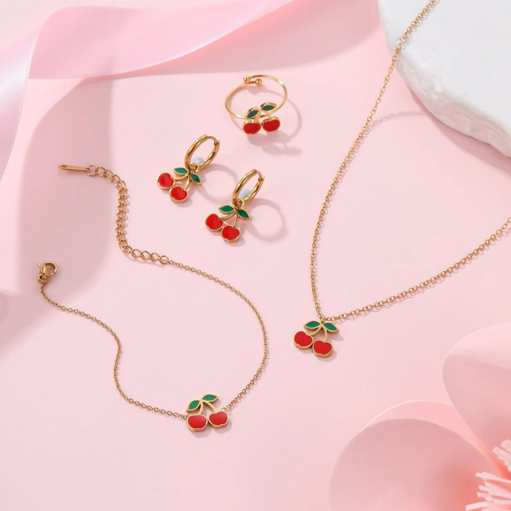 Four-piece cherry jewellery set showing necklace, bracelet, earrings, and ring with 18K electroplated finish
