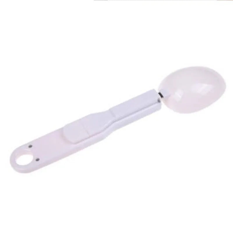 White digital kitchen spoon scale with LCD display showing 0.0g on a wooden table