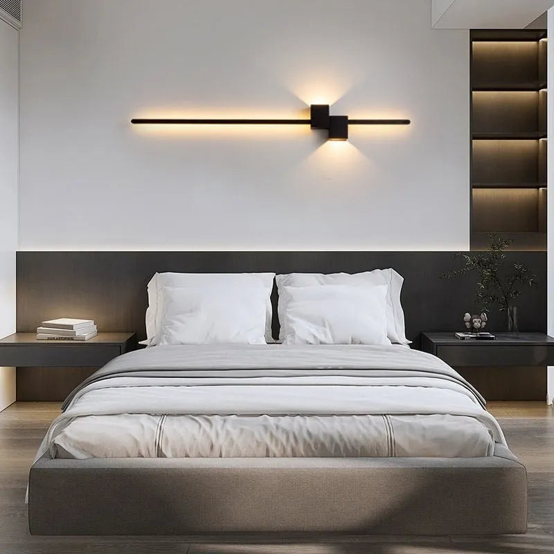 Modern minimalist wall lamp black 80cm length installed above a bedside table with warm low-voltage light