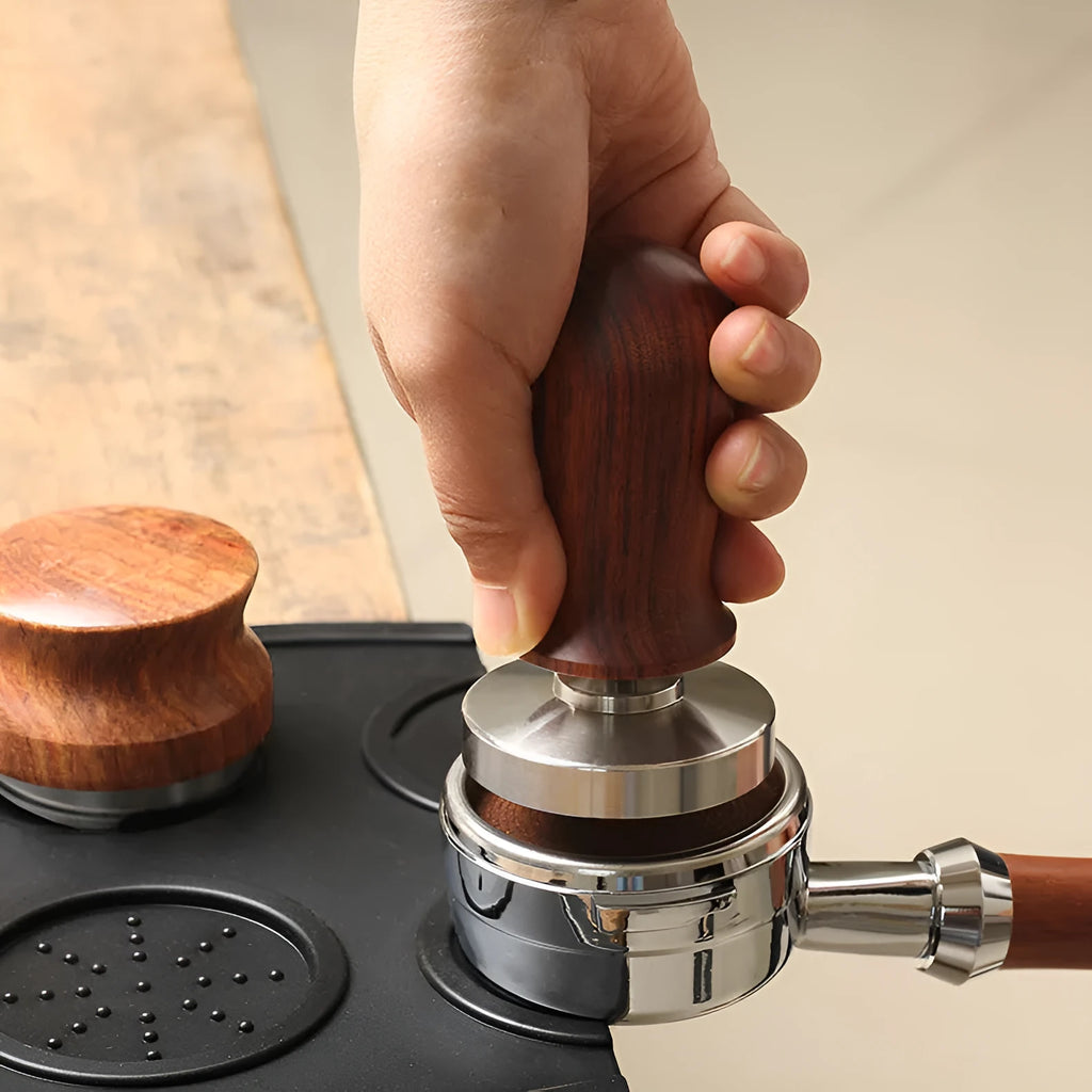 Black silicone coffee tamper pad with stainless steel base for non-slip espresso preparation.