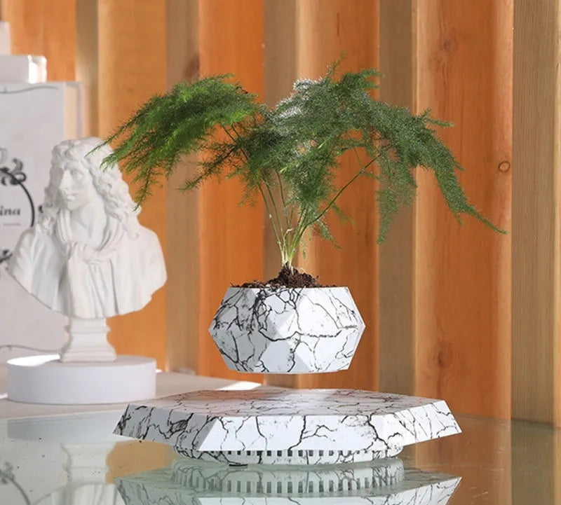Marble-coloured levitating plant pot floating above magnetic base with small plant rotating