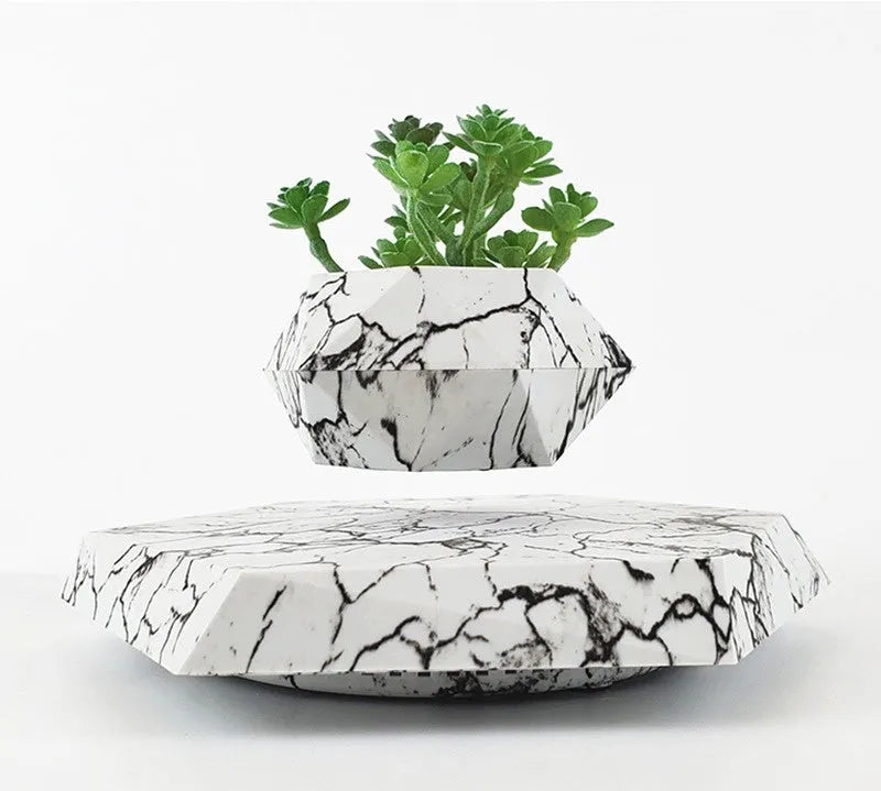 Marble-coloured levitating plant pot floating above magnetic base with small plant rotating