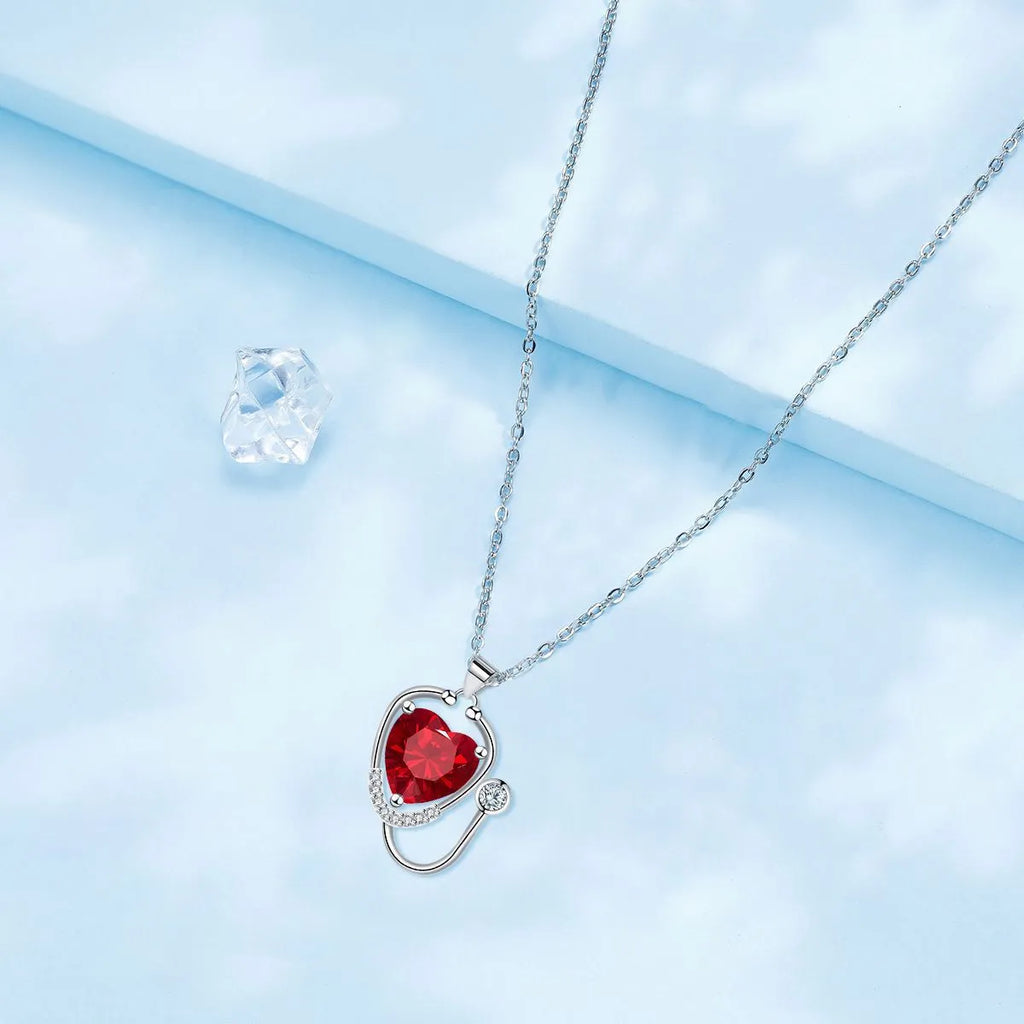 Red diamond stethoscope necklace with a wing and cross pendant on a chain.