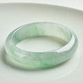 Light green jade bracelet on wrist, natural style, showing sizing scale from 53mm to 64mm