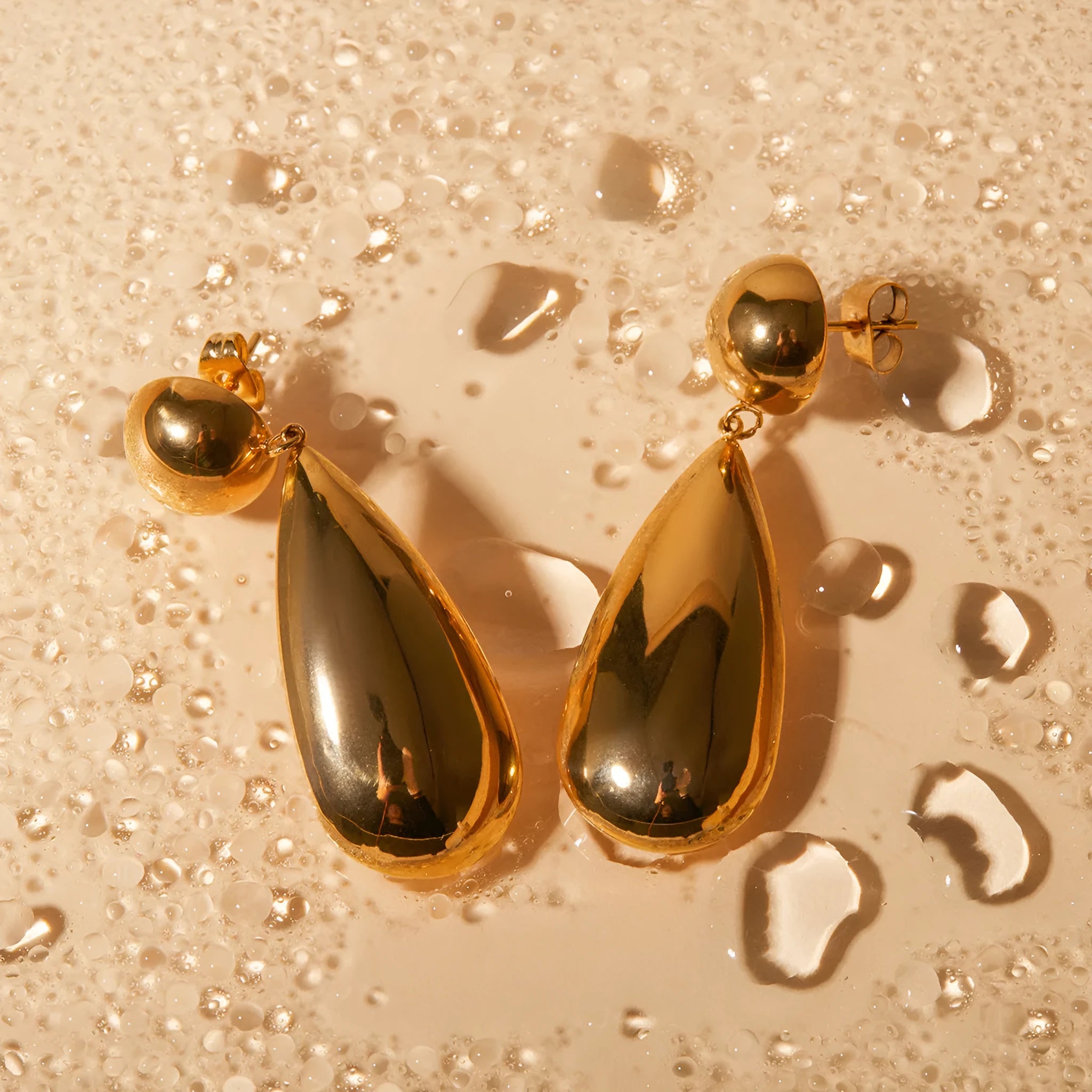 A pair of gold-coloured geometric earrings with a hemisphere base and dangling water drop pendant.