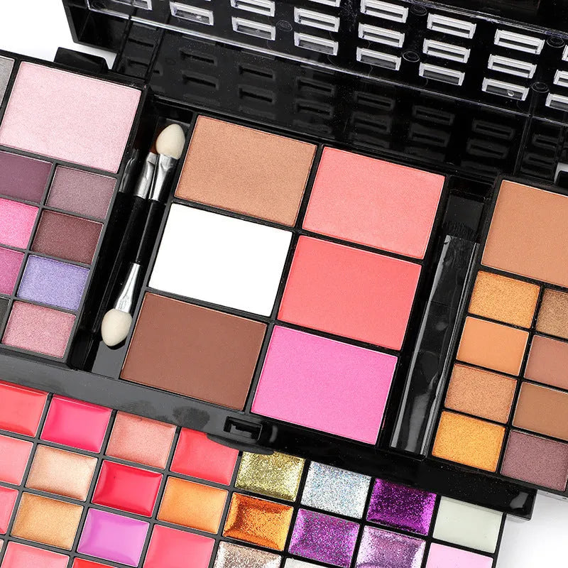 74 colour makeup palette open showing layered powder plates with eyeshadows, lip glosses, blush and contour, with mirror and brushes.
