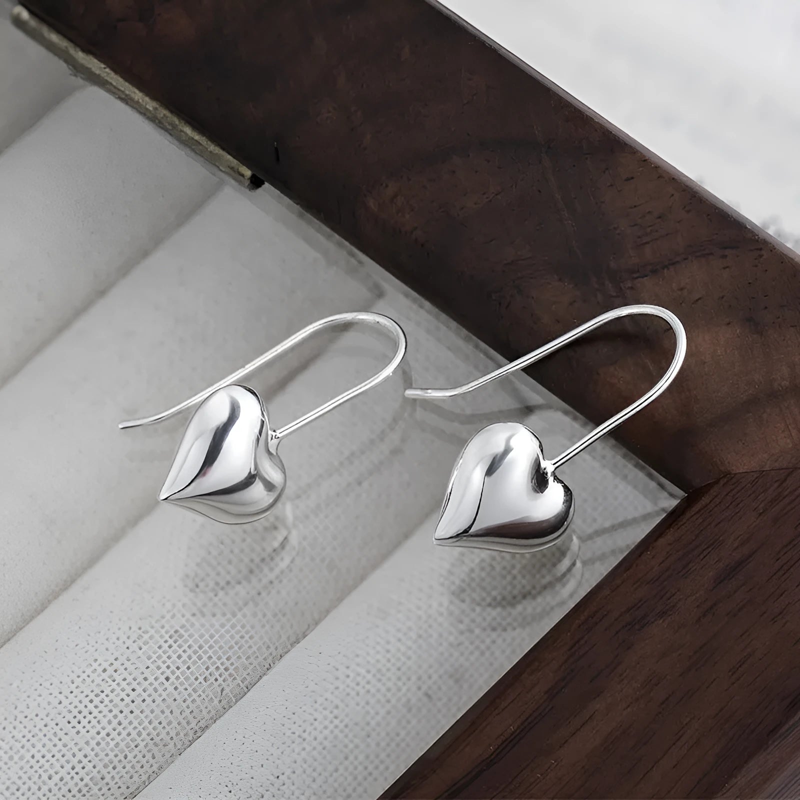 Pair of silver-tone 3D glossy heart-shaped drop earrings on a white background.