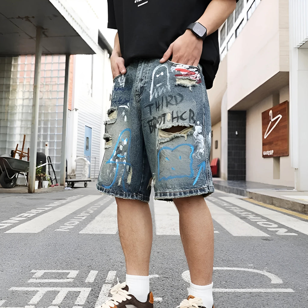 Blue denim shorts for men with rips and a graffiti pattern, featuring a zipper fly.