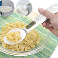 White digital kitchen spoon scale with LCD display showing 0.0g on a wooden table