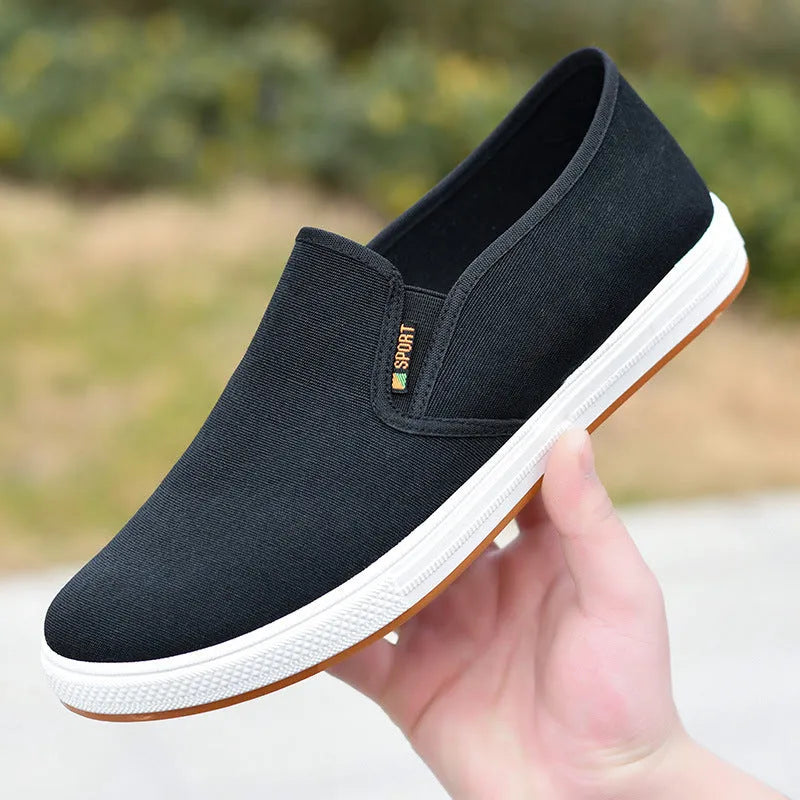 Men's black slip-on canvas trainers with round toe and low-top design on a white background