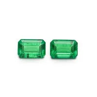 Selection of cultivated Columbia green emerald gemstones in various shapes and sizes on a white background.