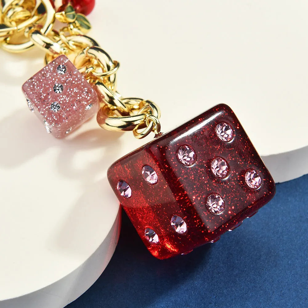 Close-up of a cherry red and white metal dice keychain pendant with a square pattern on a vintage-style suitcase charm.