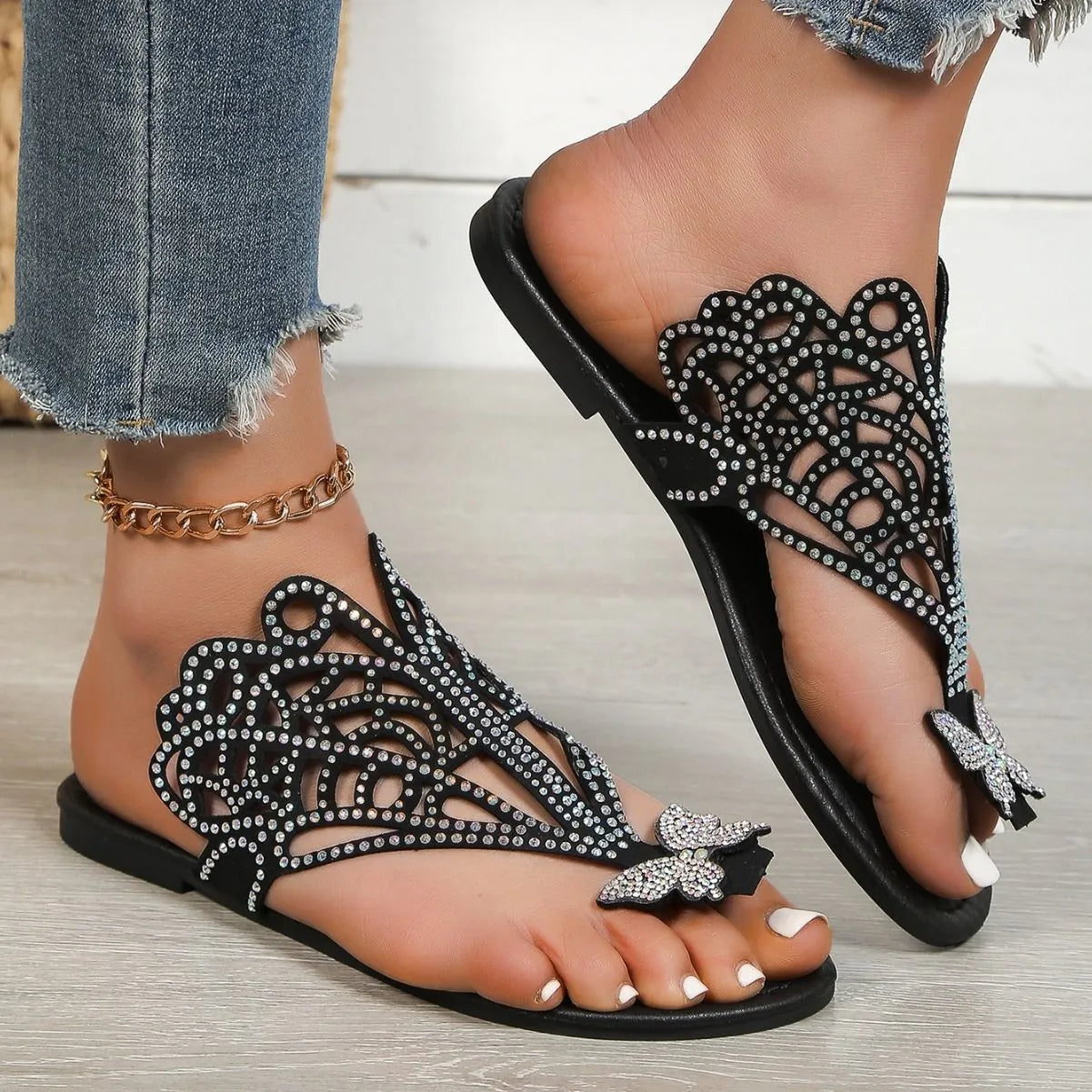 Women's black slip-on sandals with flip-toe design, rhinestone decoration, hollow-out detailing, and a flat rubber sole.