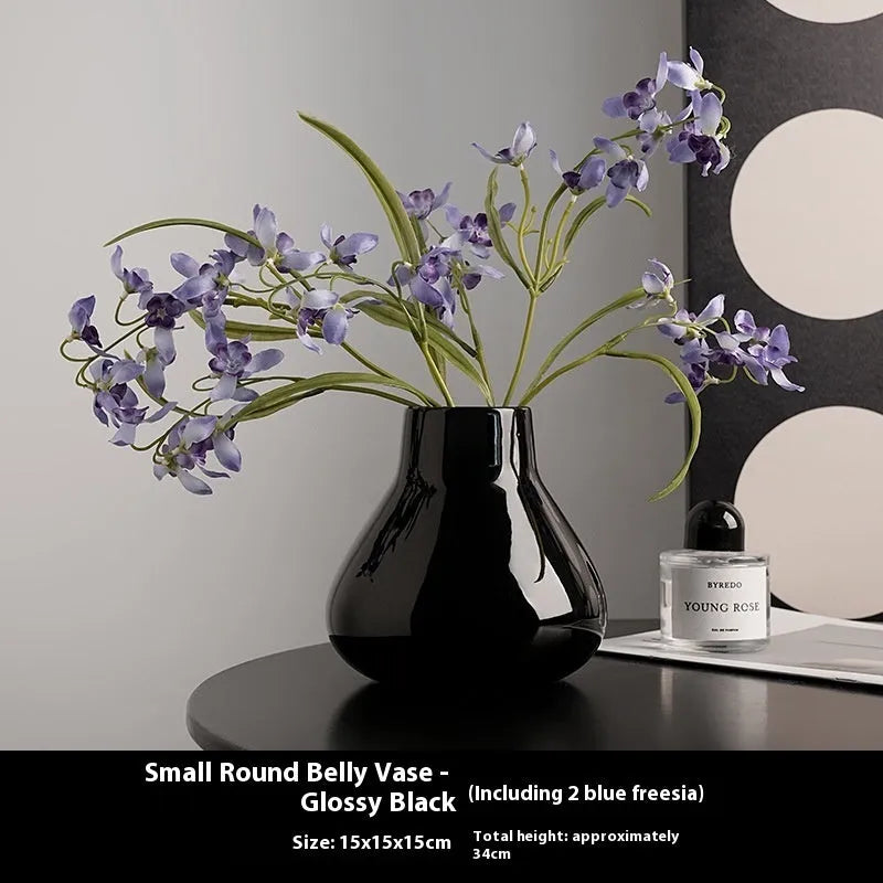 Black ceramic round belly vase with white orchid flowers on wooden shelf