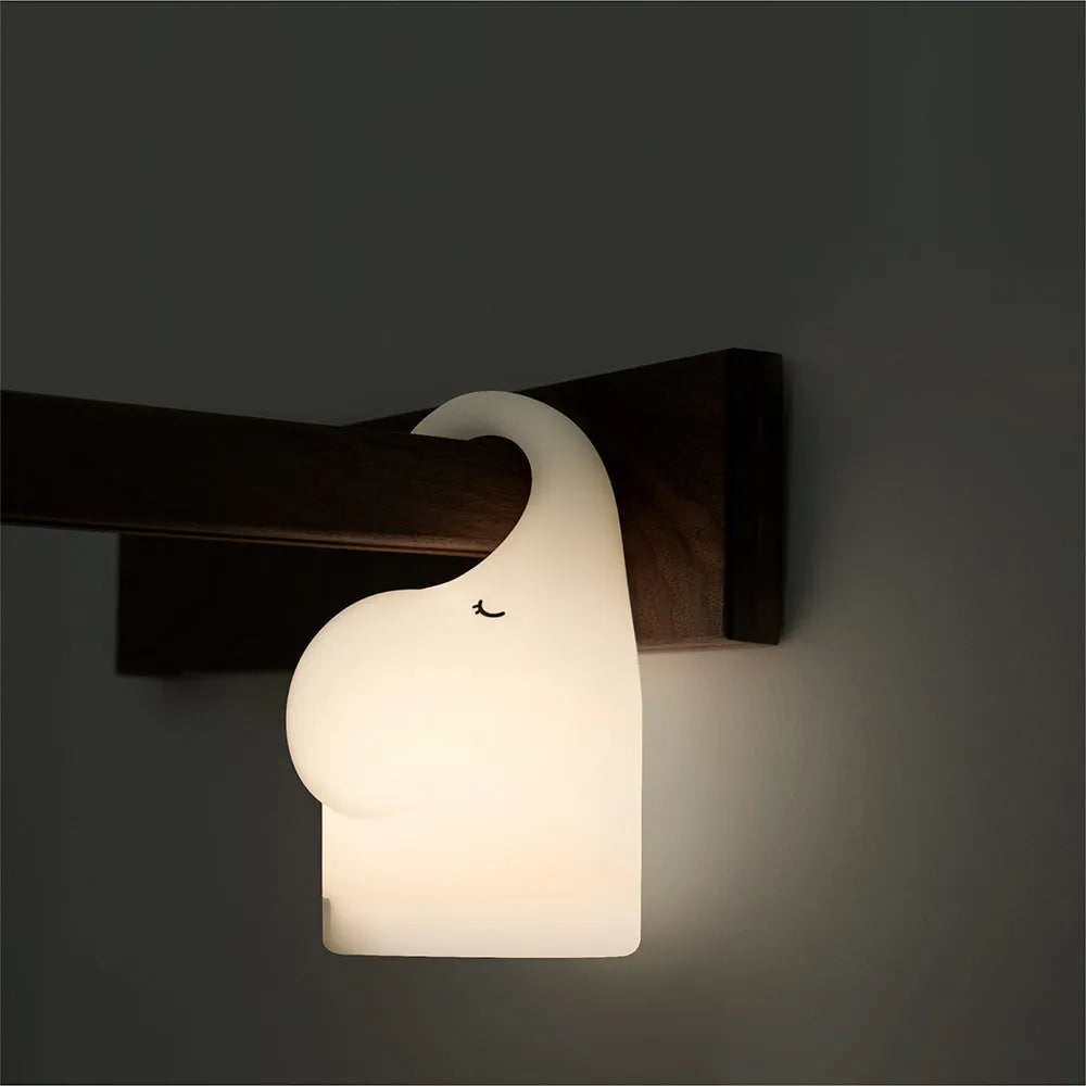 DOMI Elephant shaped silicone night light with warm white LED glow on a bedside table.