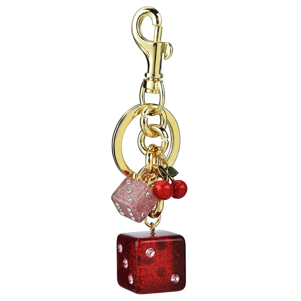 Close-up of a cherry red and white metal dice keychain pendant with a square pattern on a vintage-style suitcase charm.
