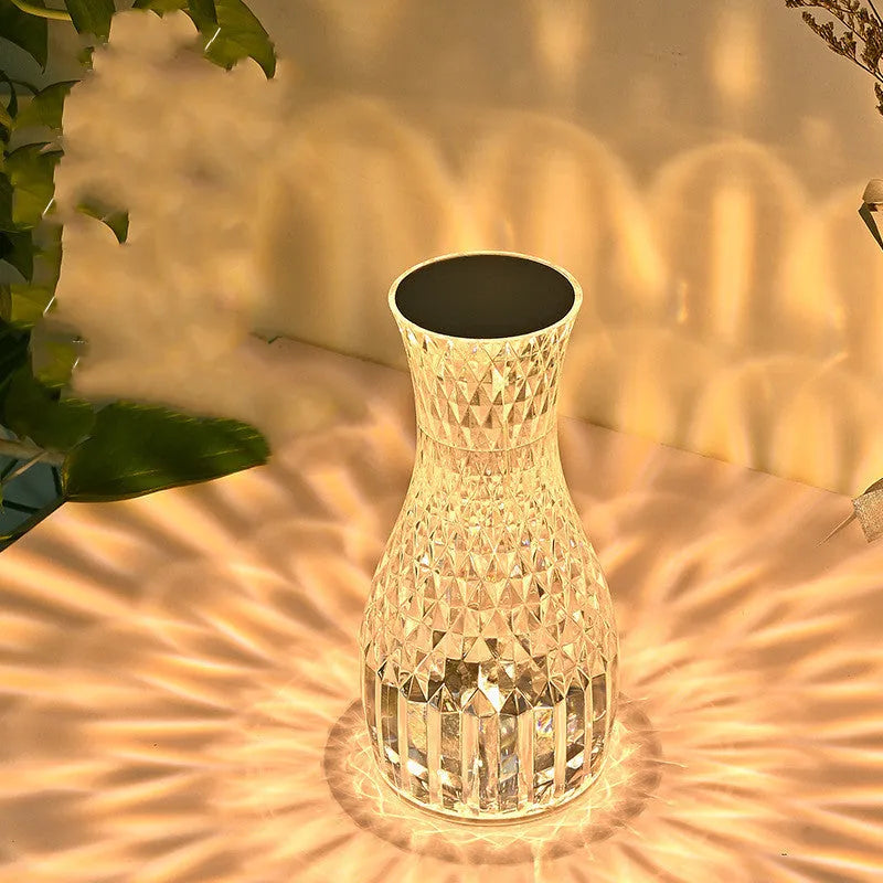 Transparent vase-shaped crystal LED table lamp on a table, showing soft coloured light.