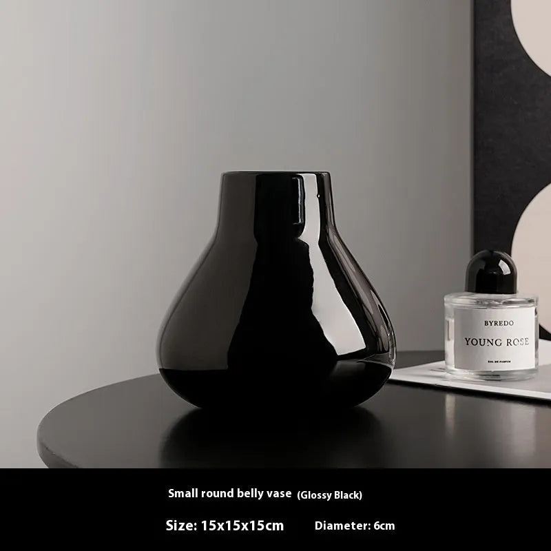 Black ceramic round belly vase with white orchid flowers on wooden shelf