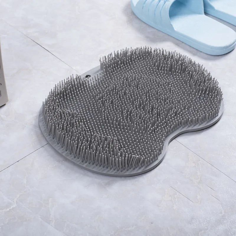 Orange non-slip massage bath brush with suction cups and soft silicone bristles on a bathroom floor.