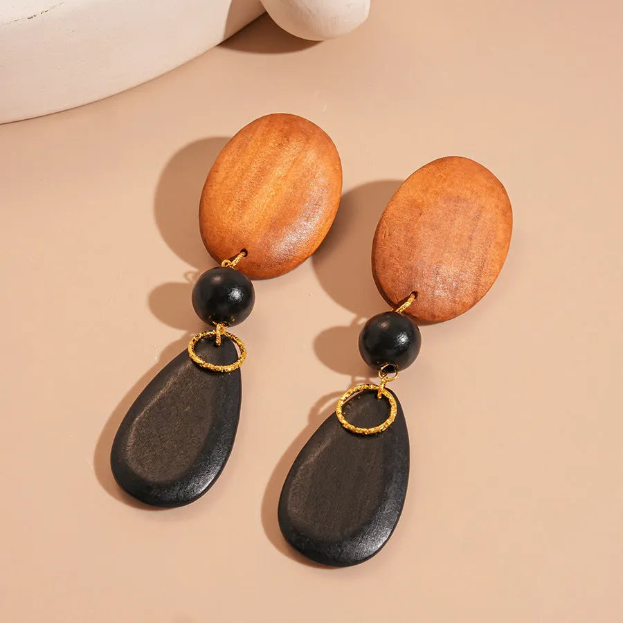 A pair of brown and black wooden ellipse earrings with a retro design on a plain background.