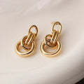 A pair of gold-coloured geometric earrings with an irregular shape on a white background.