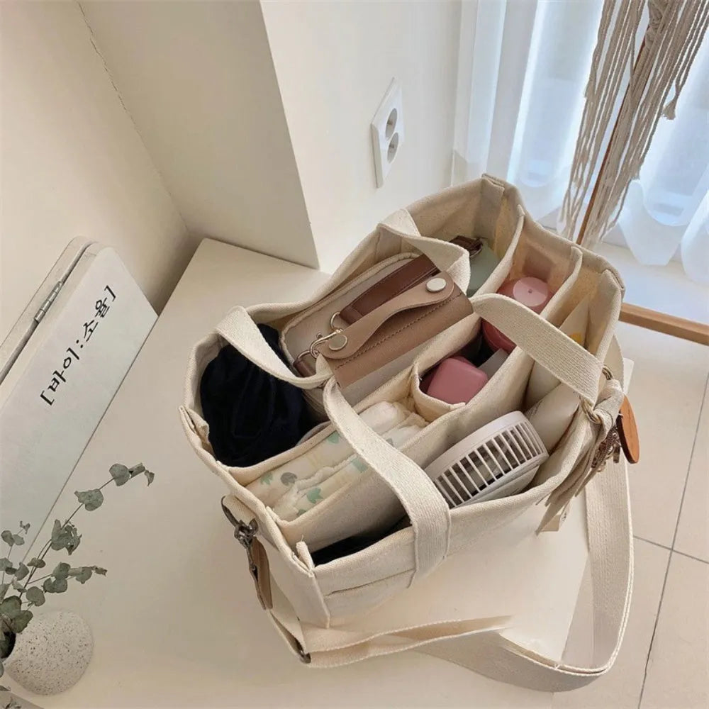 Beige canvas crossbody mommy bag holding baby bottles and wipes on table