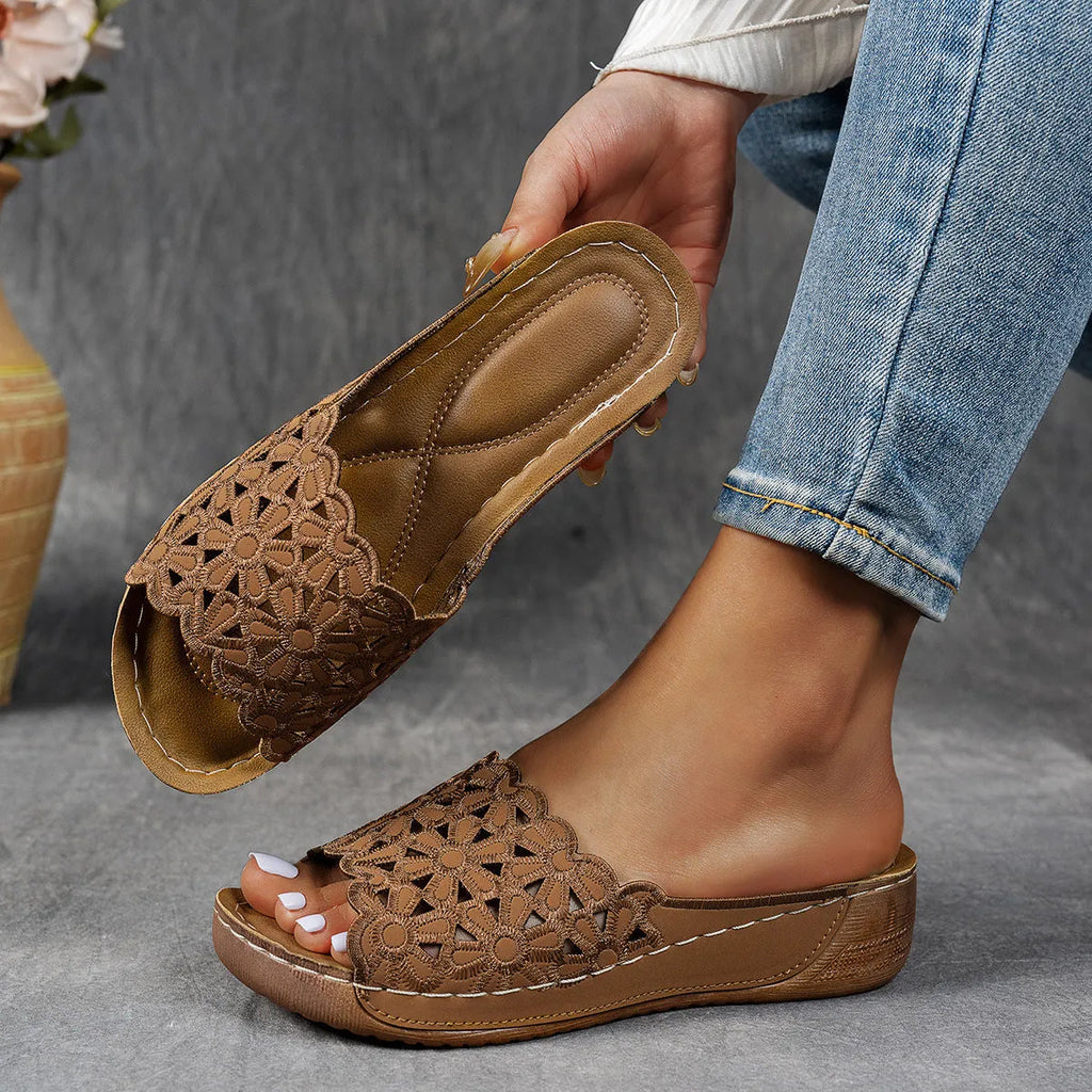 Women's black wedge beach slippers with floral cutouts on the PVC upper and a rubber sole.