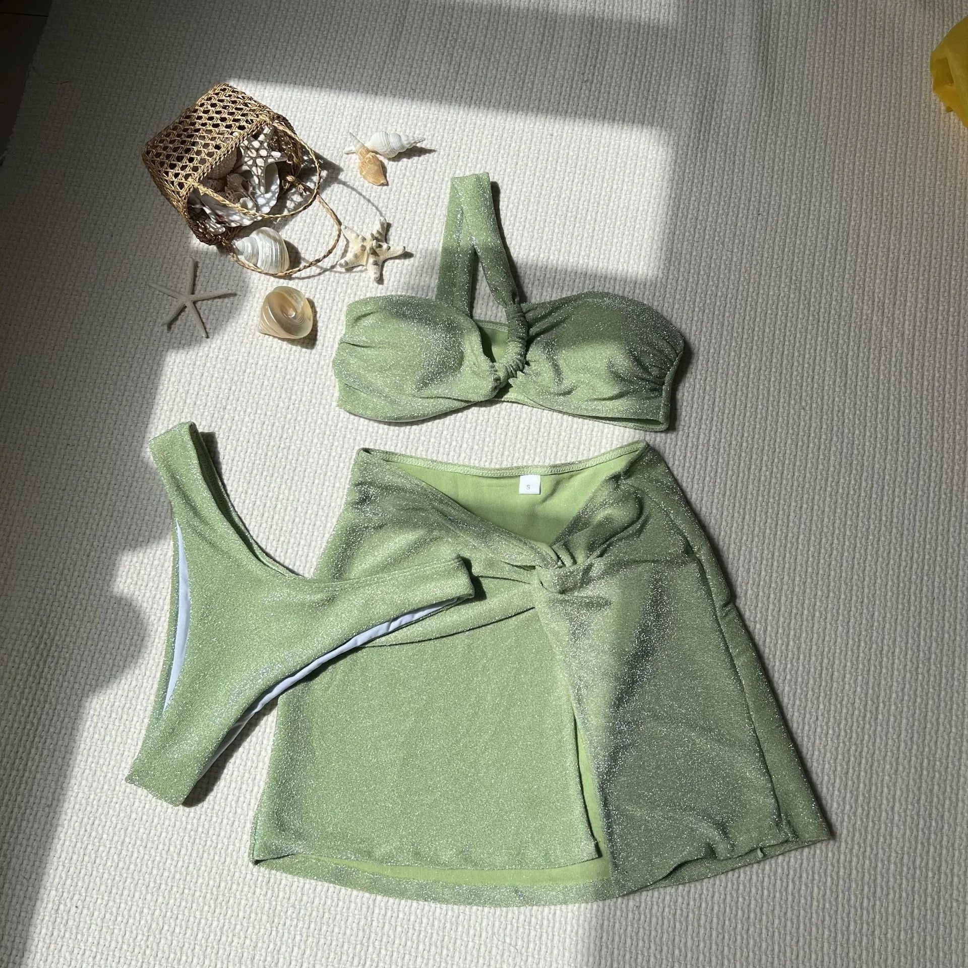 Light green one-shoulder swimsuit top with matching bikini bottoms and skirt laid flat