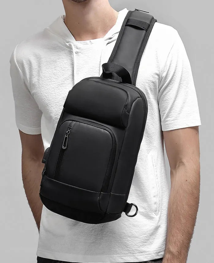 Black square-shaped outdoor shoulder bag with a single adjustable strap, shown with open zipper revealing internal laptop and phone pockets.