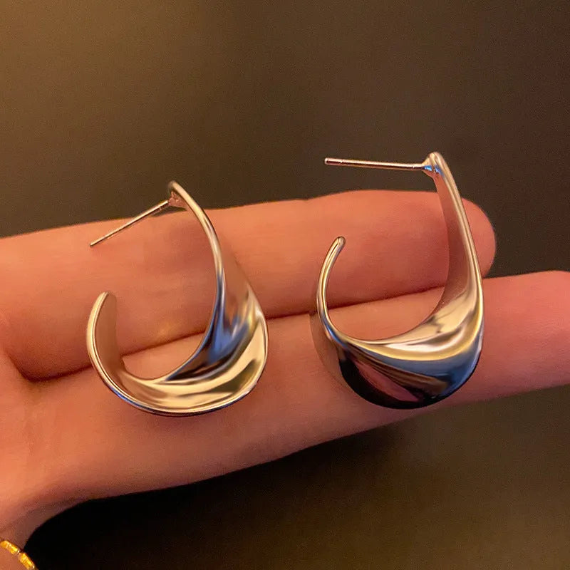 A pair of twisted geometric design metal earrings in a gold colour on a plain background