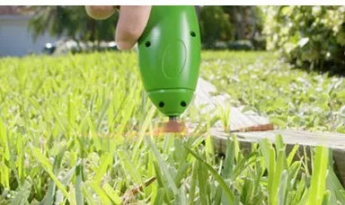 Cordless handheld grass trimmer with extension pole and protective shield on a garden lawn