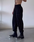 Man wearing plaid trousers with apron detailing, showing drawstring waist and multiple pockets.