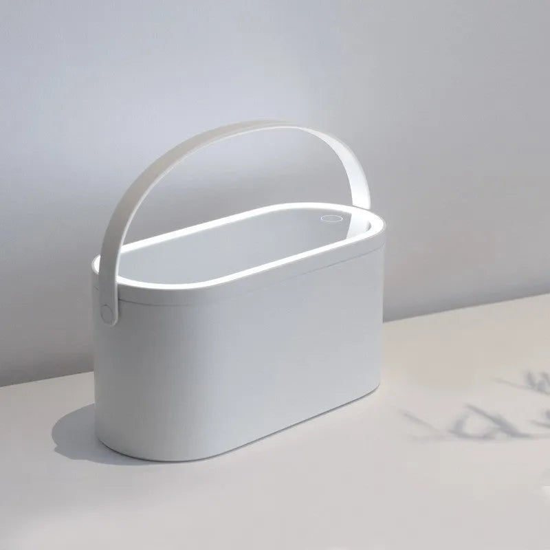 Portable LED light storage box beauty and makeup mirror with aluminium mirror lens in pink colour on a bedroom surface.