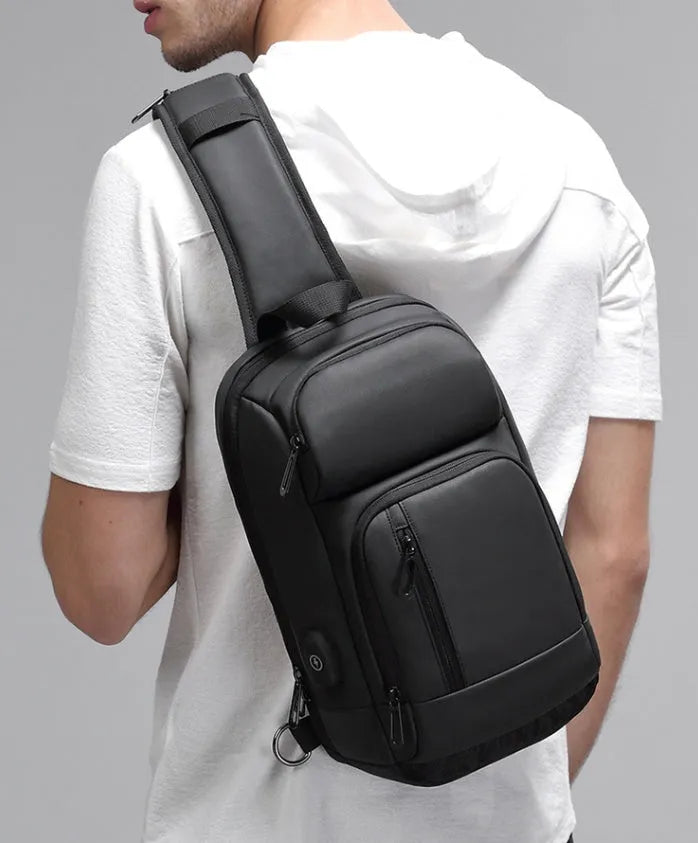 Black square-shaped outdoor shoulder bag with a single adjustable strap, shown with open zipper revealing internal laptop and phone pockets.