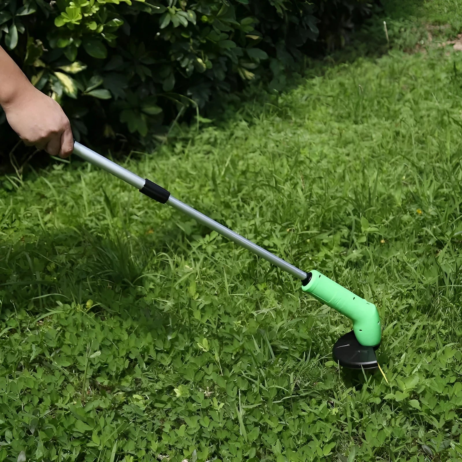 Cordless handheld grass trimmer with extension pole and protective shield on a garden lawn