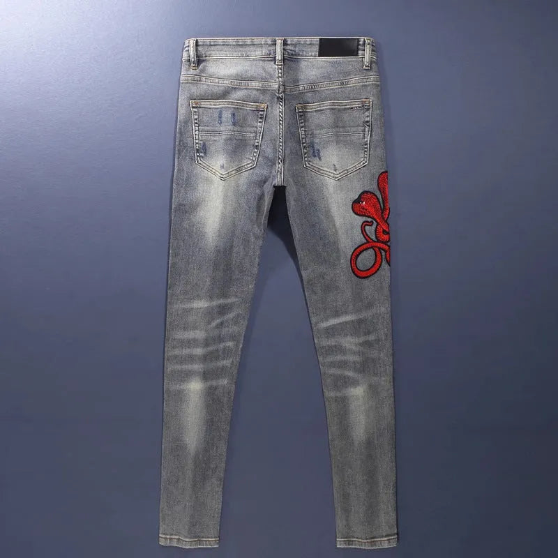 Slim-fit light blue jeans with a worn wash, knee holes, patch details, and embroidered branding on the leg.