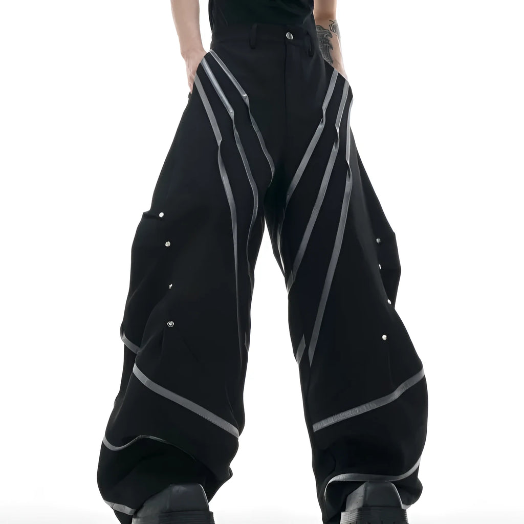 Men's black trousers with a deconstructing three-dimensional cut and pleats secured with metal striped rivets.