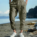 Man wearing loose khaki linen casual trousers with a drawstring waist and ankle-tied legs.