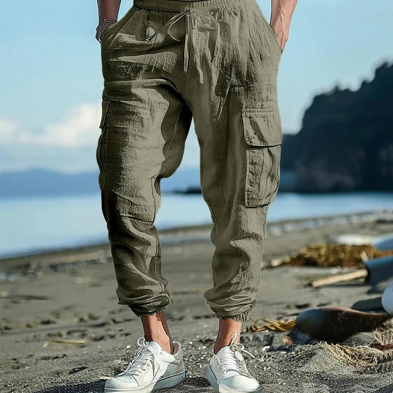 Man wearing loose khaki linen casual trousers with a drawstring waist and ankle-tied legs.