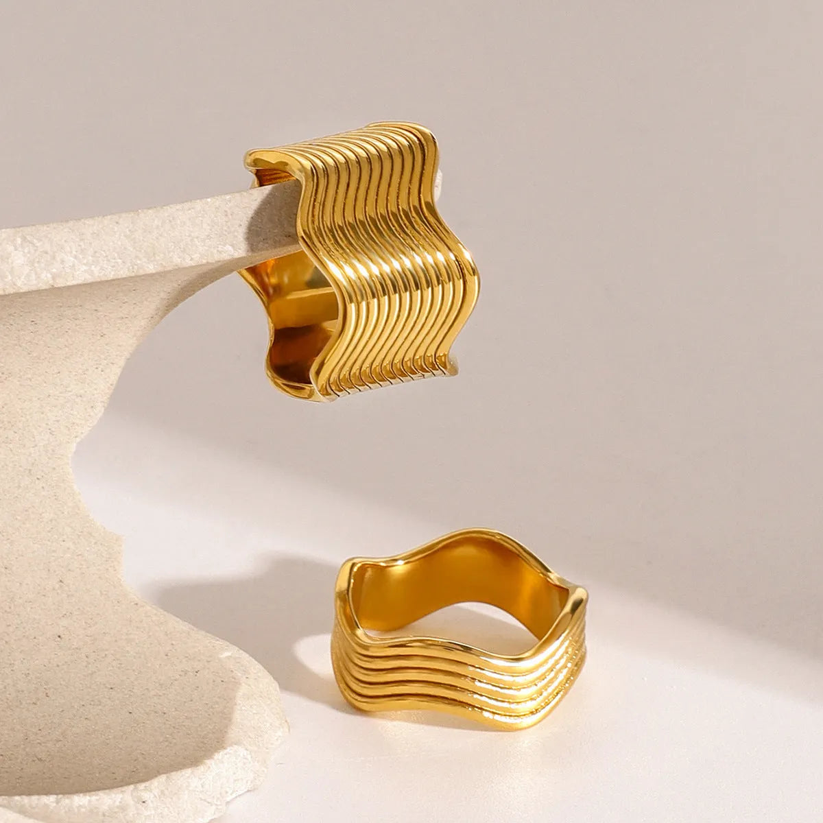 Stainless steel women's ring with wide geometric wave design in silver or rose gold tone.