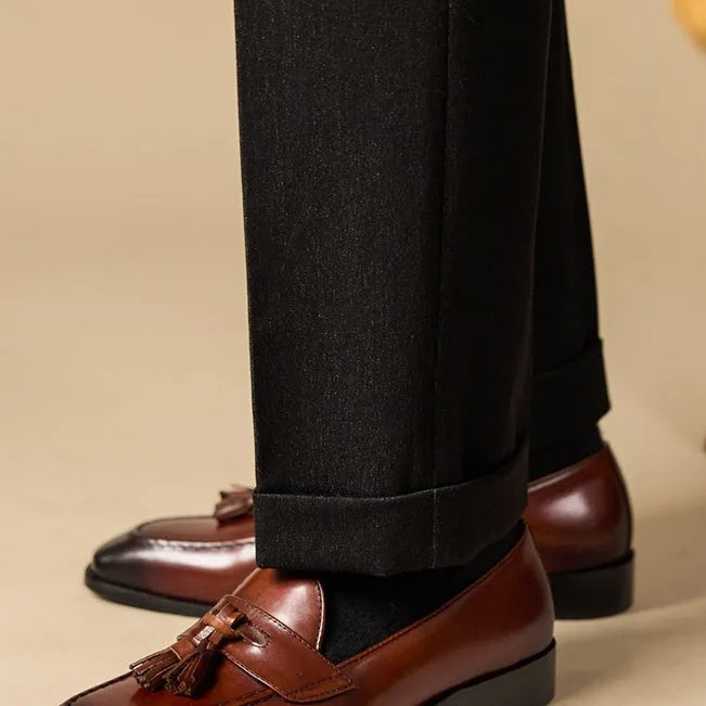 Men's black genuine leather tassel loafers on a solid background, showing polished upper and rubber sole.