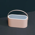 Portable LED light storage box beauty and makeup mirror with aluminium mirror lens in pink colour on a bedroom surface.