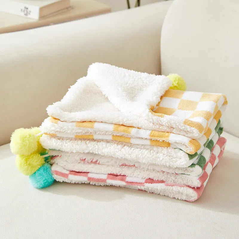 Green plaid pattern soft fleece pet blanket with fur ball decoration on a sofa