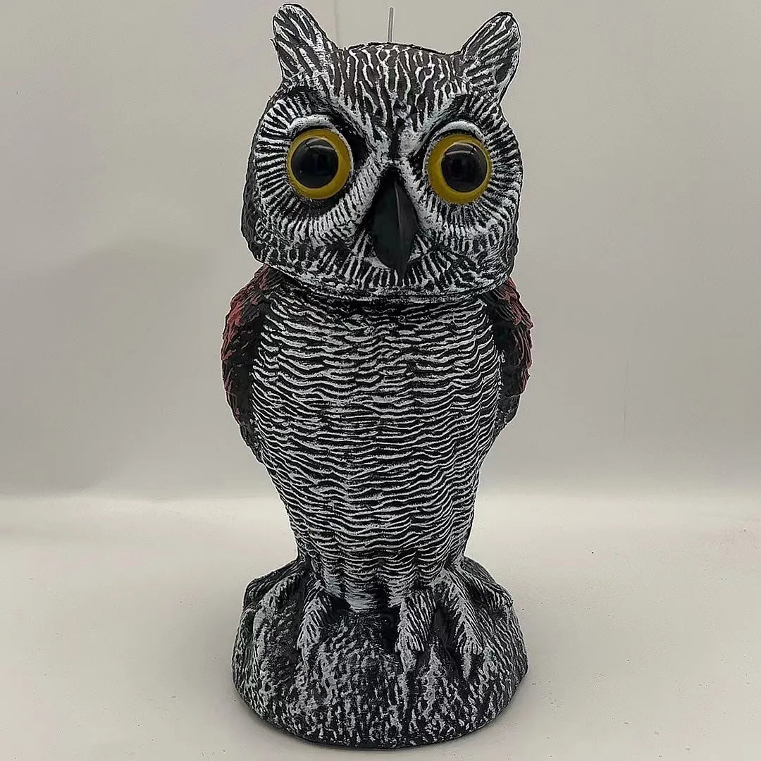 A detailed artificial owl bird scare ornament with a shaking head, shown in a garden setting.