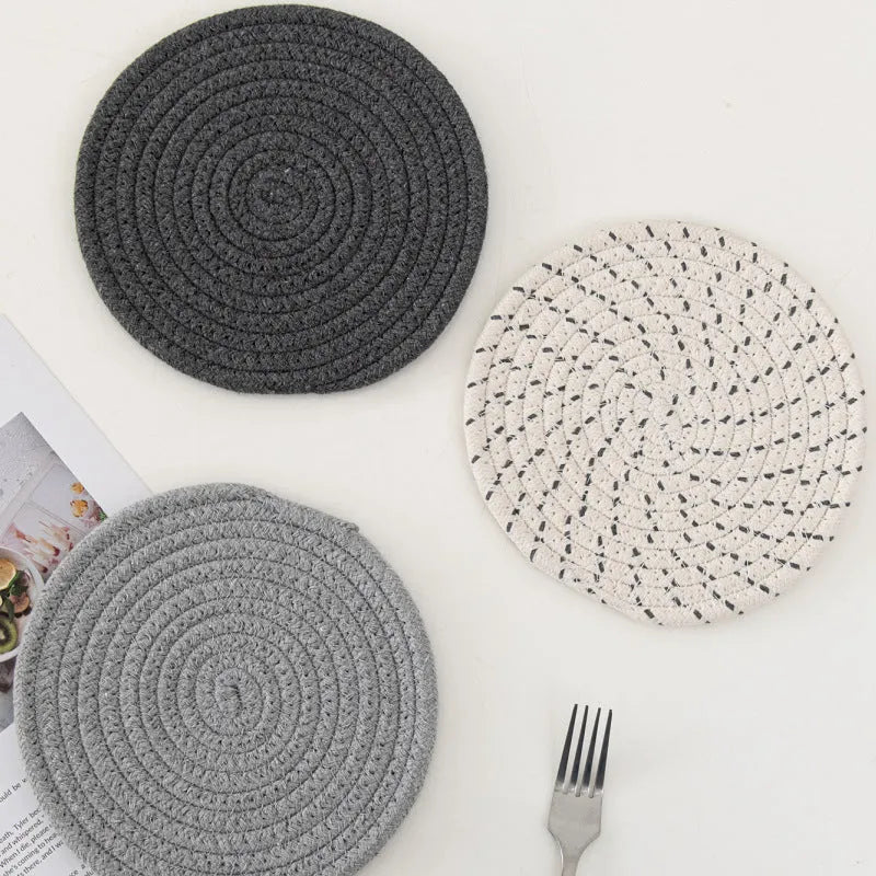 Three round grey cotton cord coasters placed on a wooden table, each 18cm in diameter.
