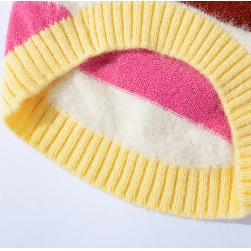Corgi dog wearing a rainbow apple striped knitted pullover sweater in brown, standing on grass