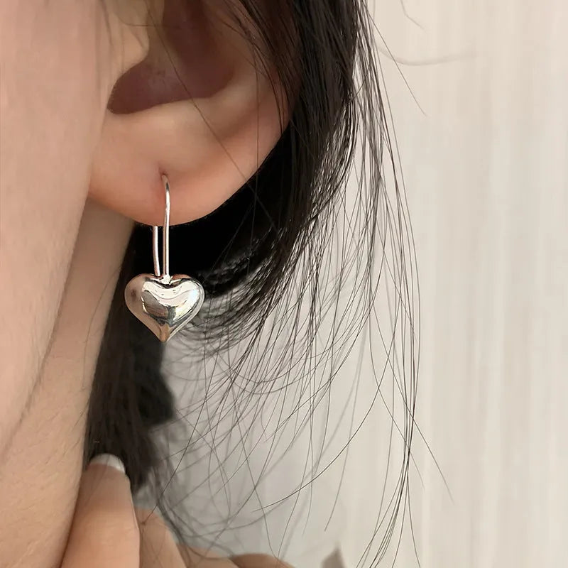 Pair of silver-tone 3D glossy heart-shaped drop earrings on a white background.