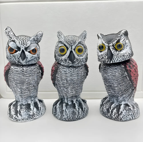 A detailed artificial owl bird scare ornament with a shaking head, shown in a garden setting.