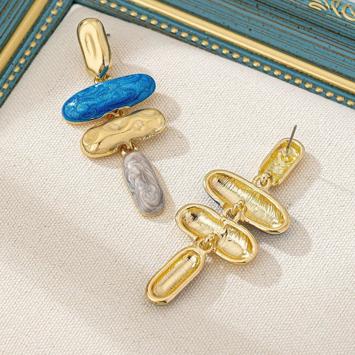 A pair of geometric-shaped stud earrings with a multicolour metallic finish on a plain background.